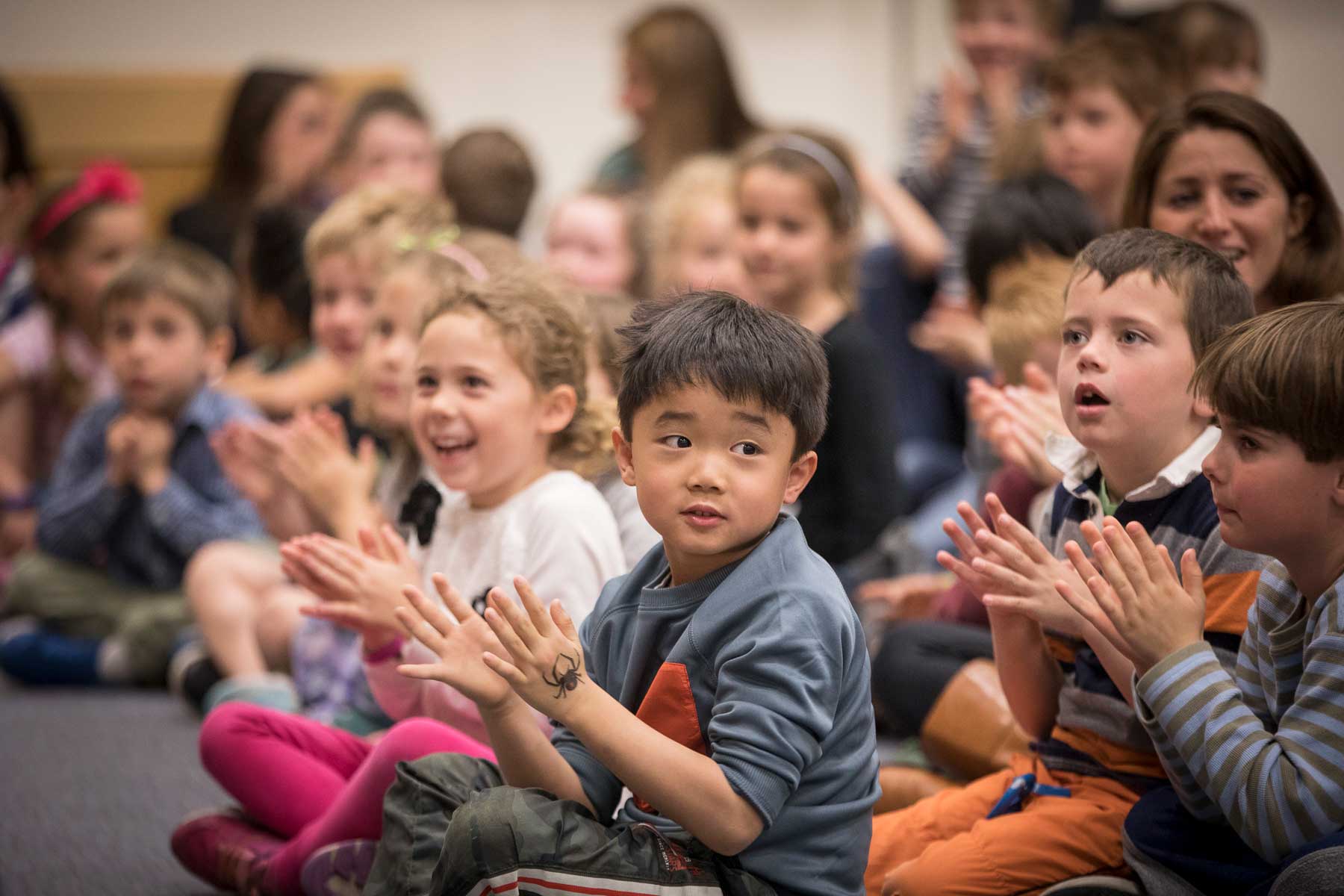 Young students sit cross-legged and clap to music