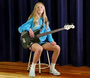 An ensembles student seated on stage with her guitar