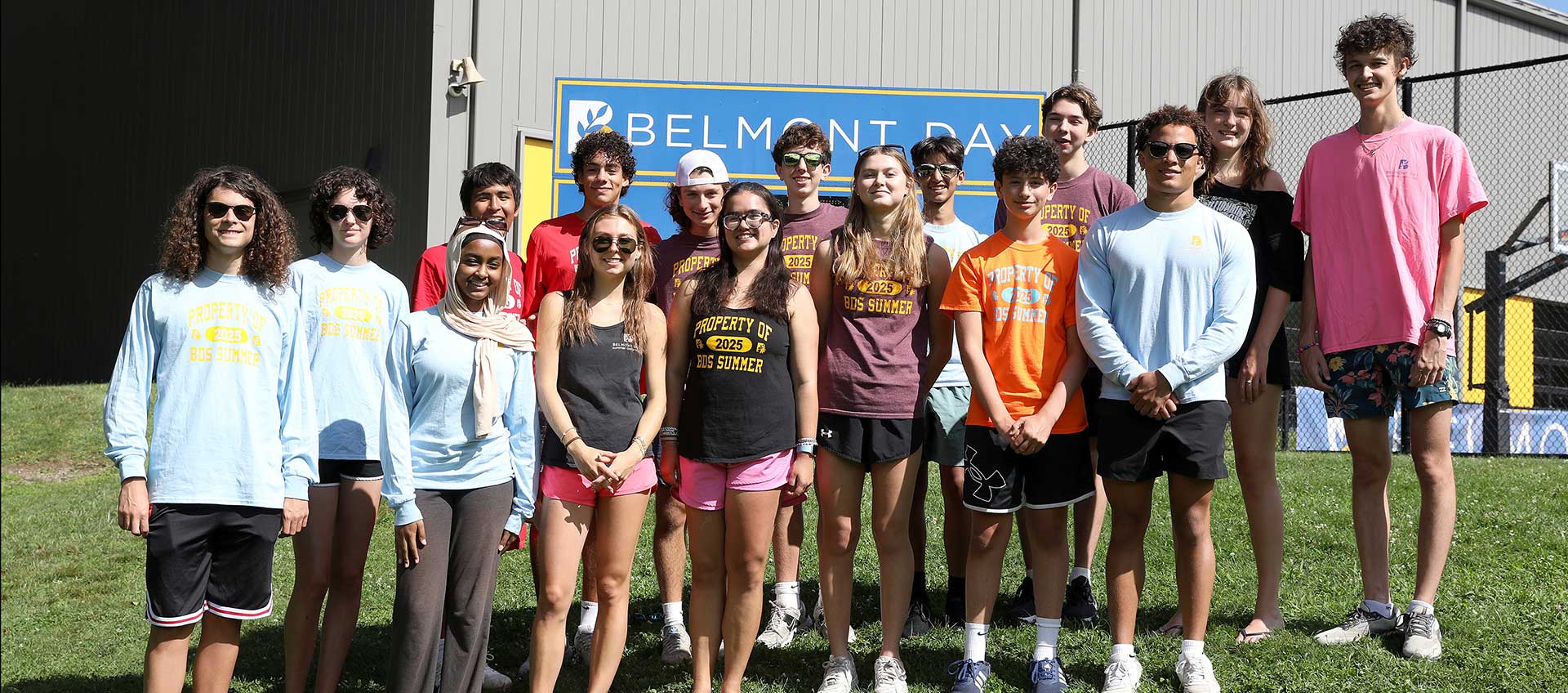 More than a dozen young alums pose in front of the BDS field scoreboard